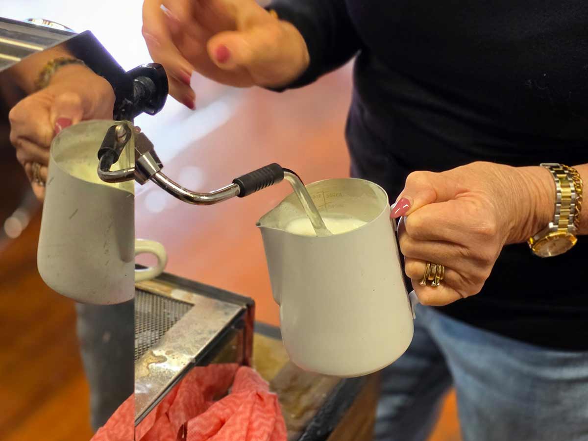 leaning how to froth milk with a milk pitcher while using an espresso machine